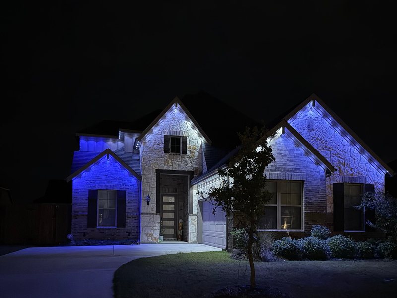 Two-story stone home lit in blue along the rooflines