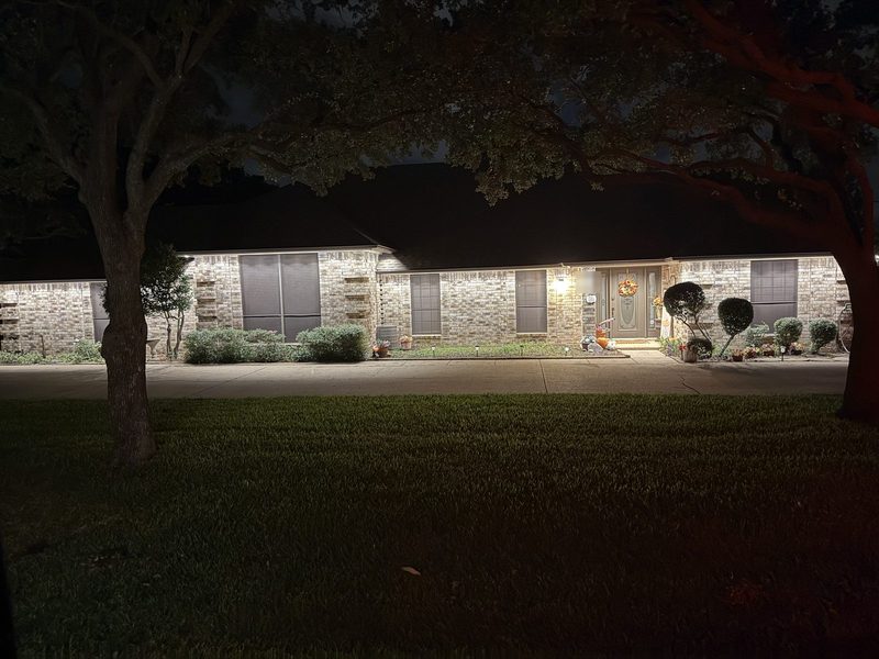 Single-story brick ranch home with warm white roofline lighting and landscape lighting