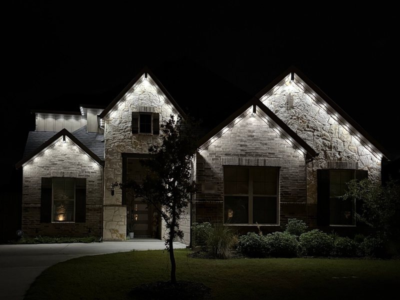 Stone and brick two-story home with warm white permanent roofline lighting along the gables