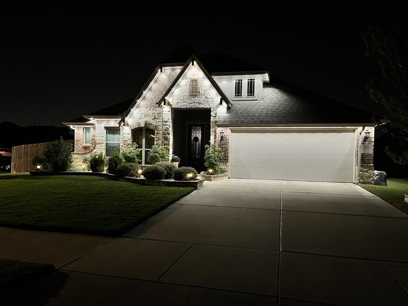 Brick and stone Fort Worth home with warm white permanent roofline lighting and landscape uplighting