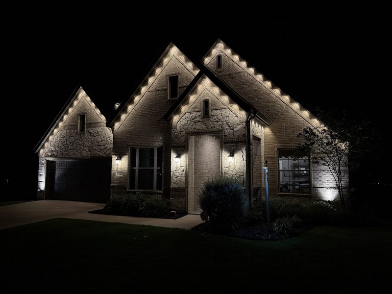 Two-story brick home with warm white permanent roofline lighting tracing every gable